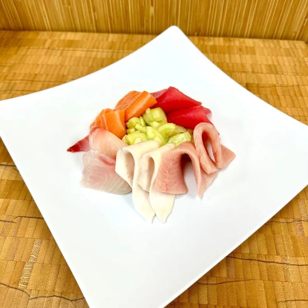 A white square plate holds a colorful assortment of fresh Sawara Sushi sashimi and green cucumber.