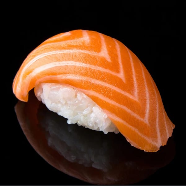 A single piece of Sawara Sushi salmon nigiri with white rice on a dark reflective surface.