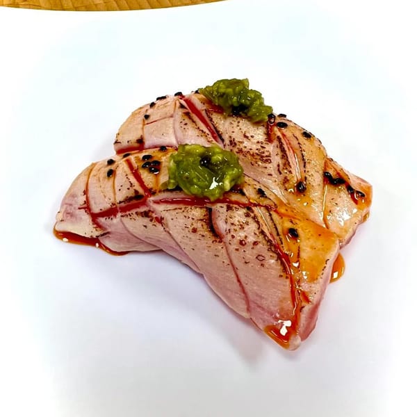 Two pieces of seared tuna sushi with green topping and dark sauce on a white plate.